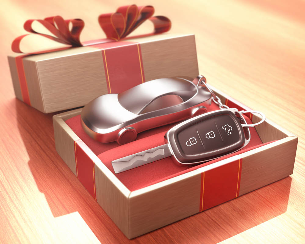 Shutterstock_315320798 Car key inside a gift box with a red ribbon tied up on the cover. Depth of field with focus on the key button.