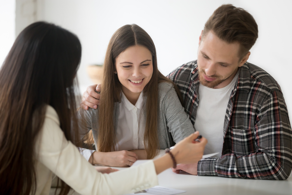 Shutterstock_1063889183 Millennial couple considering mortgage investment loan, planning wedding at meeting with financial advisor realtor planner, young smiling clients customers thinking of buying real estate or insurance