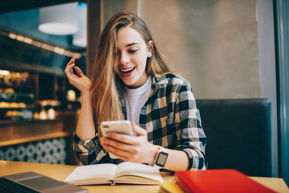 Shutterstock_1135452353 Wonder amazed hipster girl received text message on mobile phone about upcoming discounts, surprised female student chatting with friends and reading shocked news during studying at cafeteria