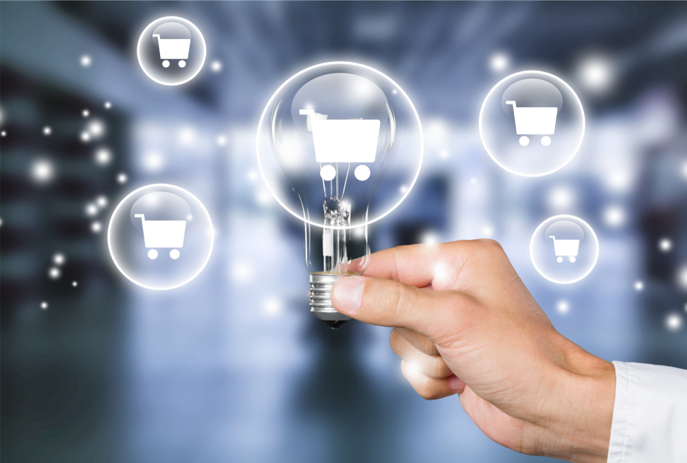 A man's hand holding a light bulb on blurred background with a shopping illustration