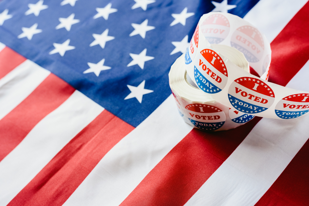 Shutterstock_1428892934 I vote today stickers roll, in US elections on American flag.