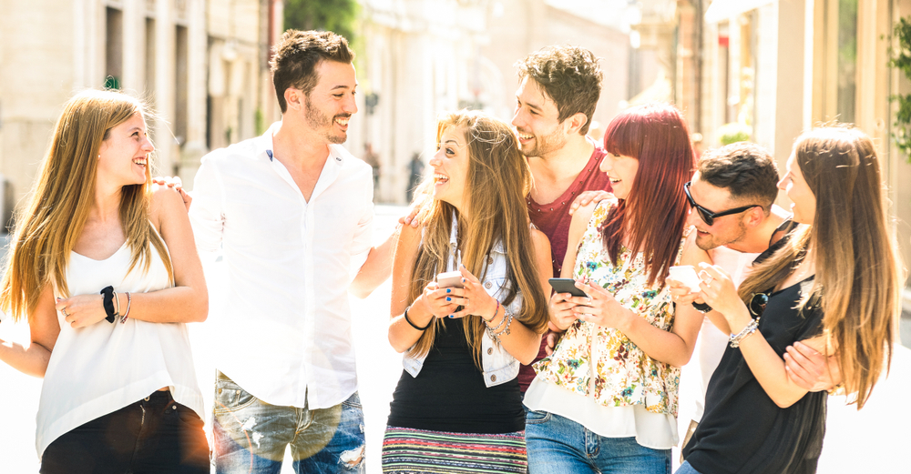 Shutterstock_1276934041 Best friends group having fun together on city street - Technology interaction concept in everyday lifestyle with millenials and gen z young people talking and using mobile smart phone