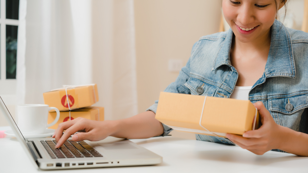 Shutterstock_ 1461739997 Beautiful smart Asian young entrepreneur business woman owner of SME online checking product on stock and save to computer working at home. Small business owner at home office concept.