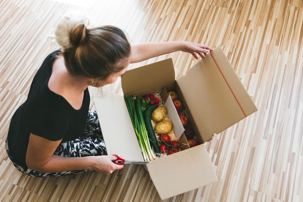 Shutterstock_491848777 woman opening a vegetable delivery box at home, online ordering