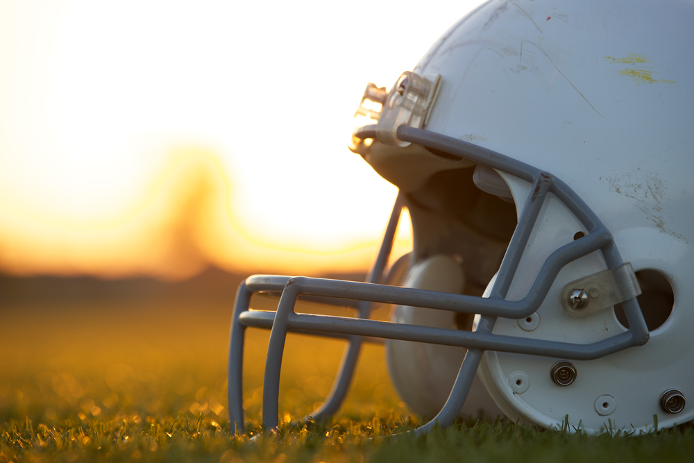 Shutterstock_149768081 American Football Helmet on the Field at Sunset with room for copy