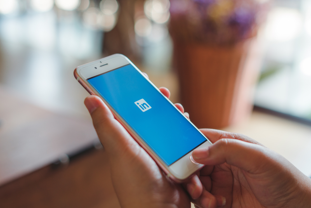 Shutterstock_ 1460740661 Woman holding Apple iPhone 6S Rose Gold with Linkedin application on the screen in coffee shop.