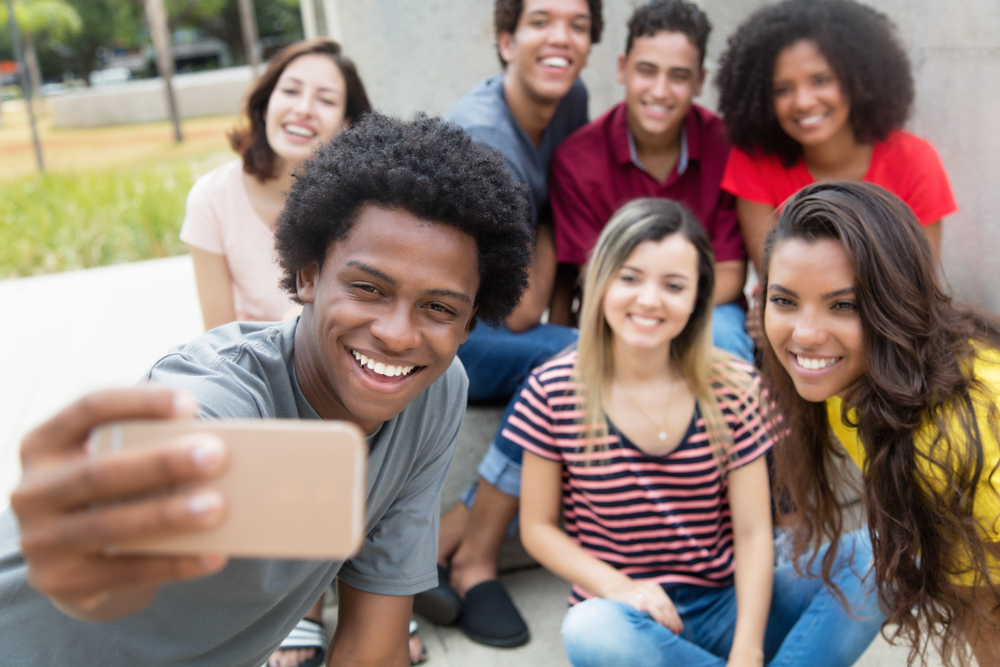 Shutterstock_765053950 Large group of international young adults taking selfie with phone outdoor in the summer