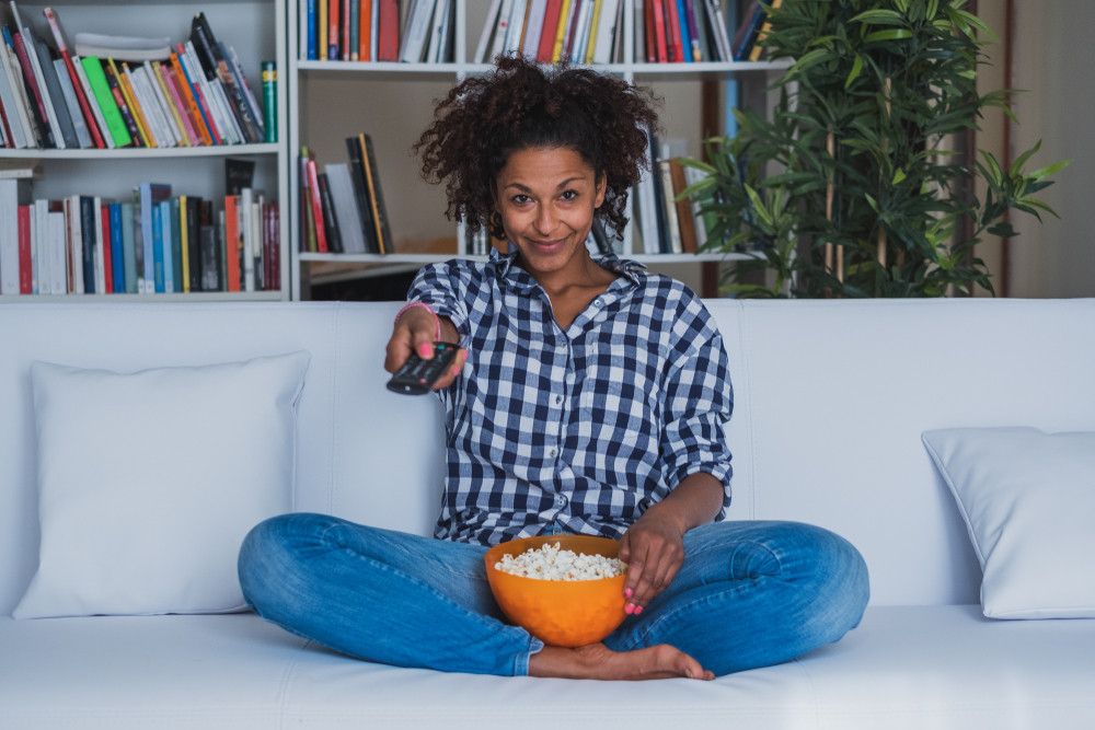 Shutterstock_1201292863 Happy woman sitting at home with remote control watching tv