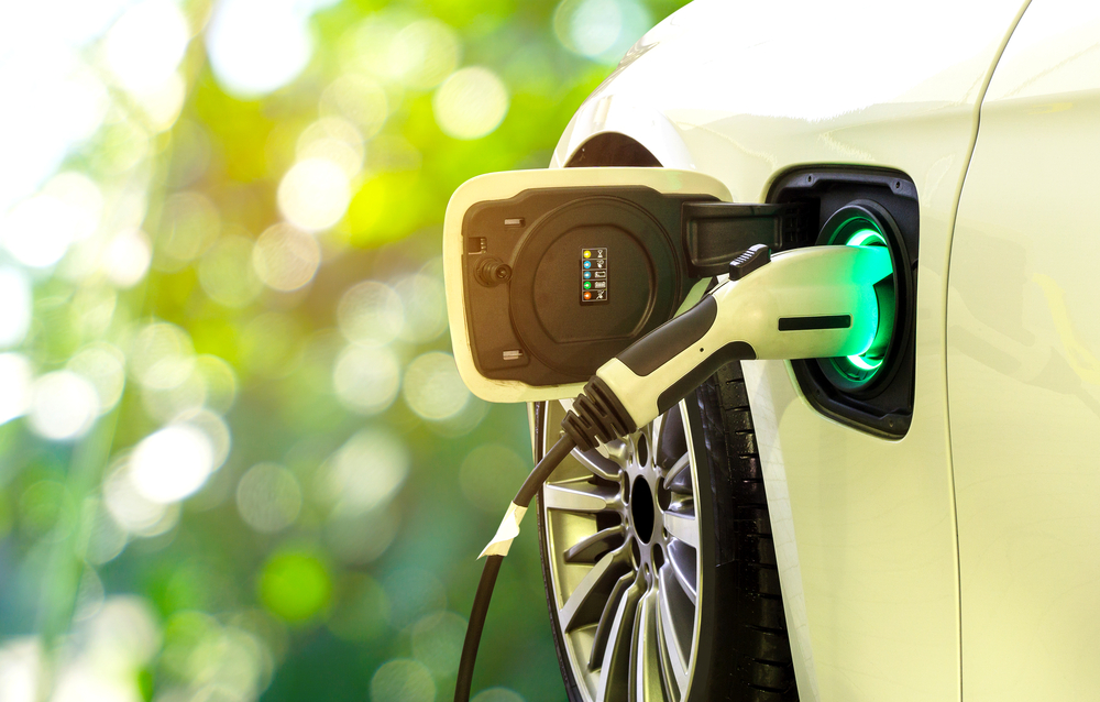 Shutterstock_750610873 EV Car or Electric car at charging station with the power cable supply plugged in on blurred nature with soft light background. Eco-friendly alternative energy concept