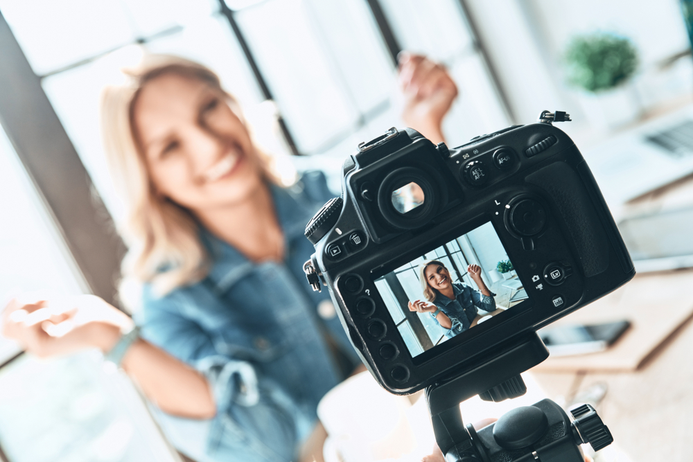 shutterstock_1099279586  Filming. Beautiful young woman in casual wear smiling while recording video