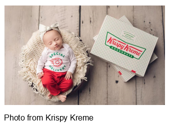 Baby sleeping in a basket in a special delivery shirt next to boxes of krispy kreme