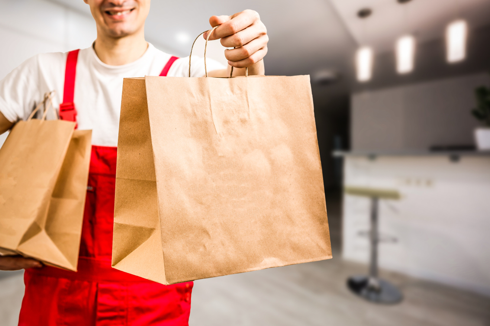 shutterstock_1459738184 Diverse of paper containers for takeaway food. Delivery man is carrying