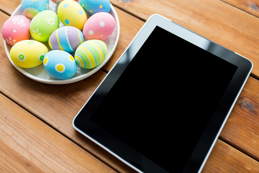 Shutterstock_374875450 Easter, holidays, technology, advertisement and object concept - close up of colored easter eggs on plate and blank tablet pc computer