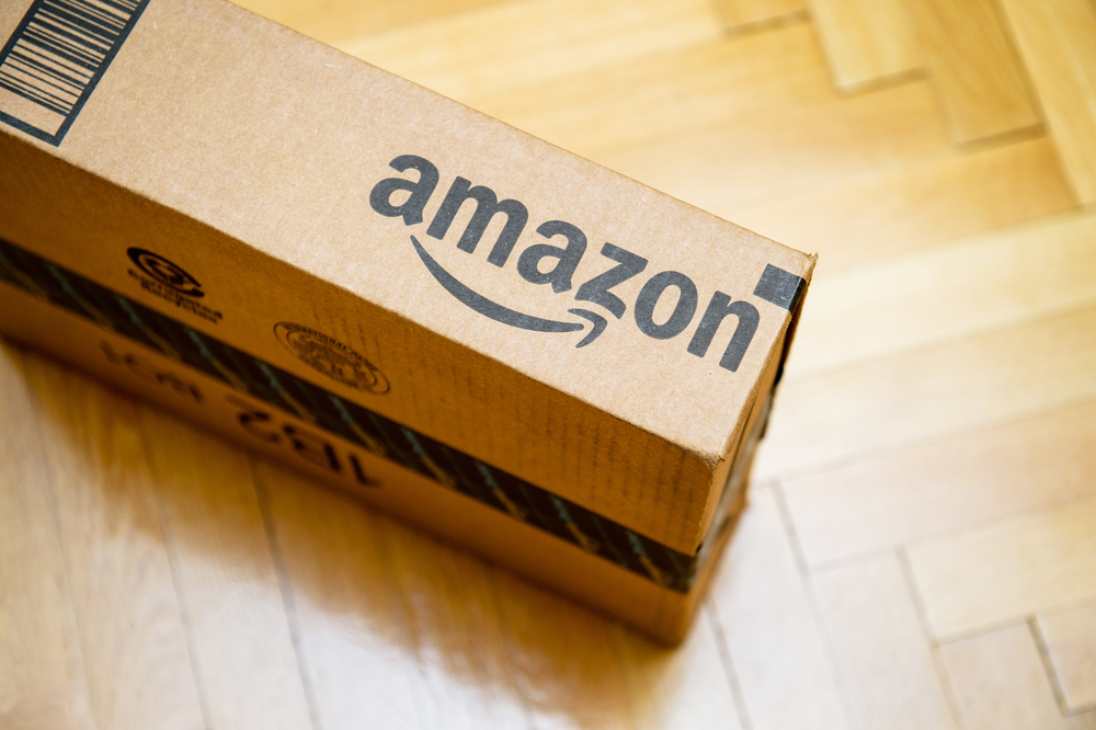 Shutterstock_373709401 PARIS, FRANCE - JAN 28, 2016: Amazon logotype printed on cardboard box side seen from above on a wooden parwuet floor. Amazon is an American electronic e-commerce company distribution worlwide