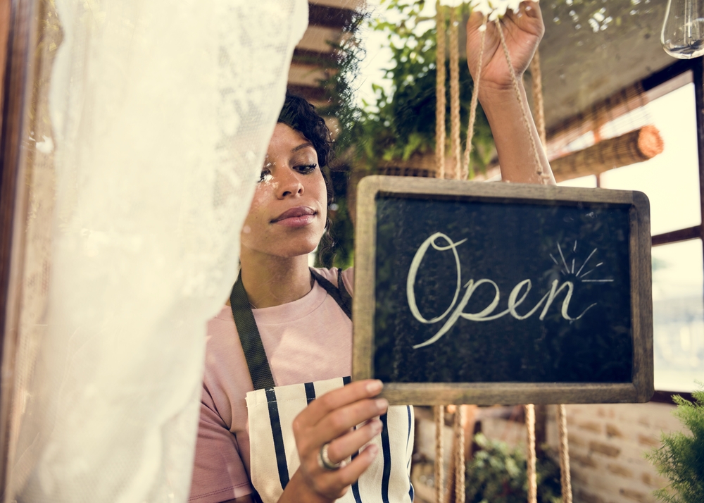 Shutterstock_593517713 Woman Hanging Open Sign by the Glass Window