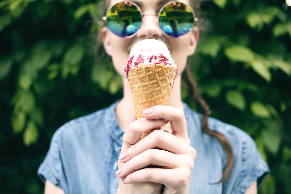 Shutterstock_426670690 Outdoor closeup fashion portrait of young hipster crazy girl eating ice cream in summer hot weather in round mirror sunglasses have fun and good mood. Toned style instagram filters