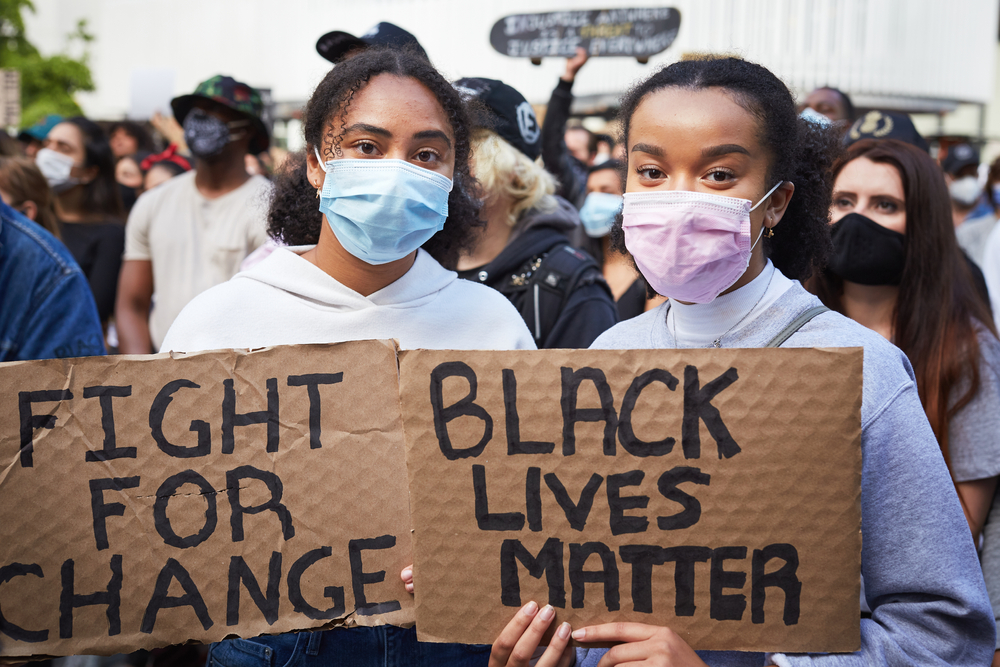 Shutterstock_1746891338 Vancouver BC, Canada, May 31 2020: Portrait of two young women of dark skin colour with a face mask holding cardboard banners "black lives matter"