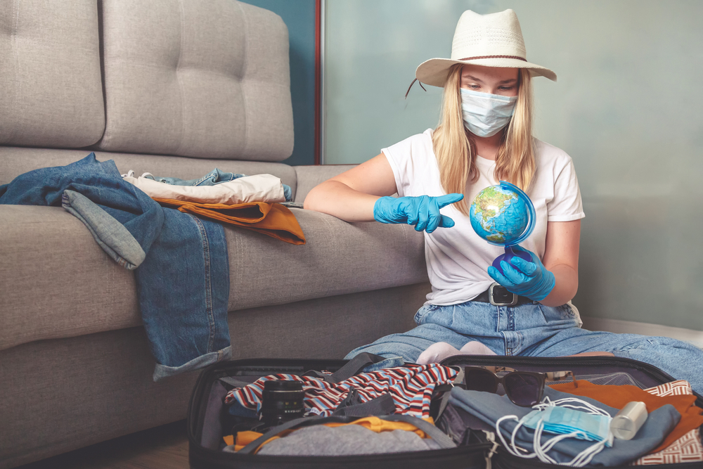 Shutterstock_1767283199 Travel. masked girl puts her things in a suitcase and dreams of rest, traveling after quarantine, blocking, covert 19. Staycation.local travel.Tourism after opening borders, end of quarantine