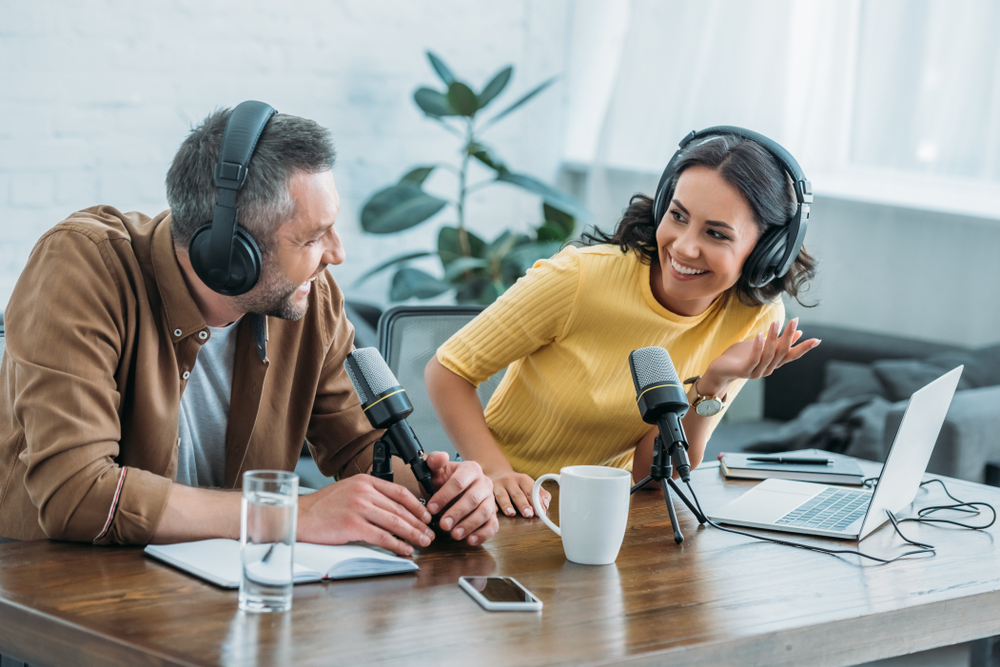 Shutterstock_1433456504 two radio hosts in headphones laughing while recording podcast in studio together