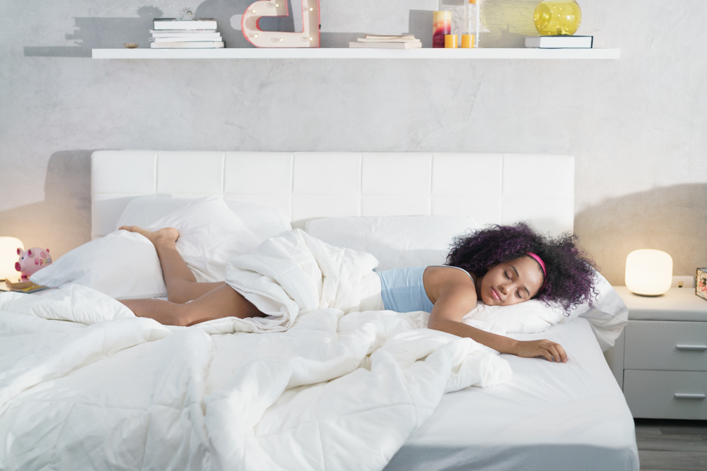 Shutterstock_1091314463 Young African American woman waking up at home. Portrait of happy black girl smiling, enjoying a large king size mattress all for herself.