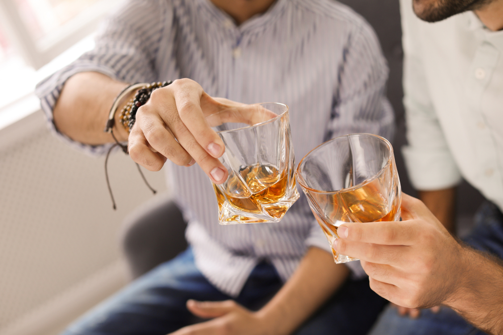 Shutterstock_1250604211 Friends toasting with glasses of whiskey indoors, closeup