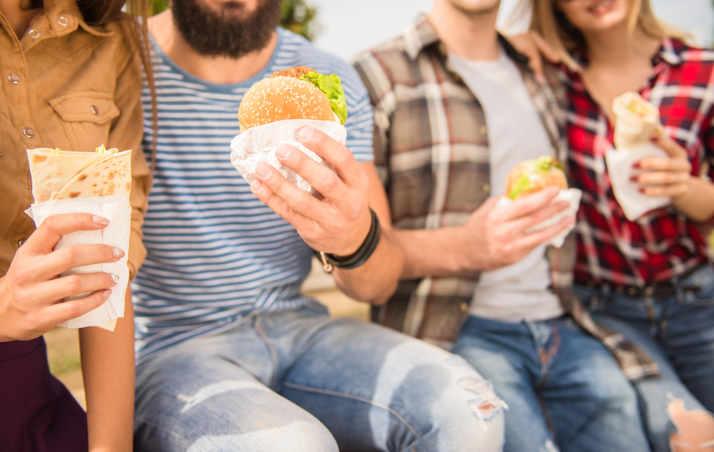 Shutterstock_321206387 Young people walking outdoors. Sitting in the park and eat fast food