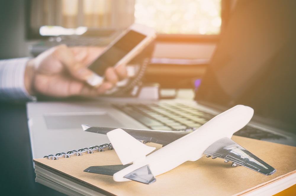 Shutterstock_568310371 Business man is making call in office for global communication. A man holding mobile phone with Airplane on for ground for Business travel communication concept.