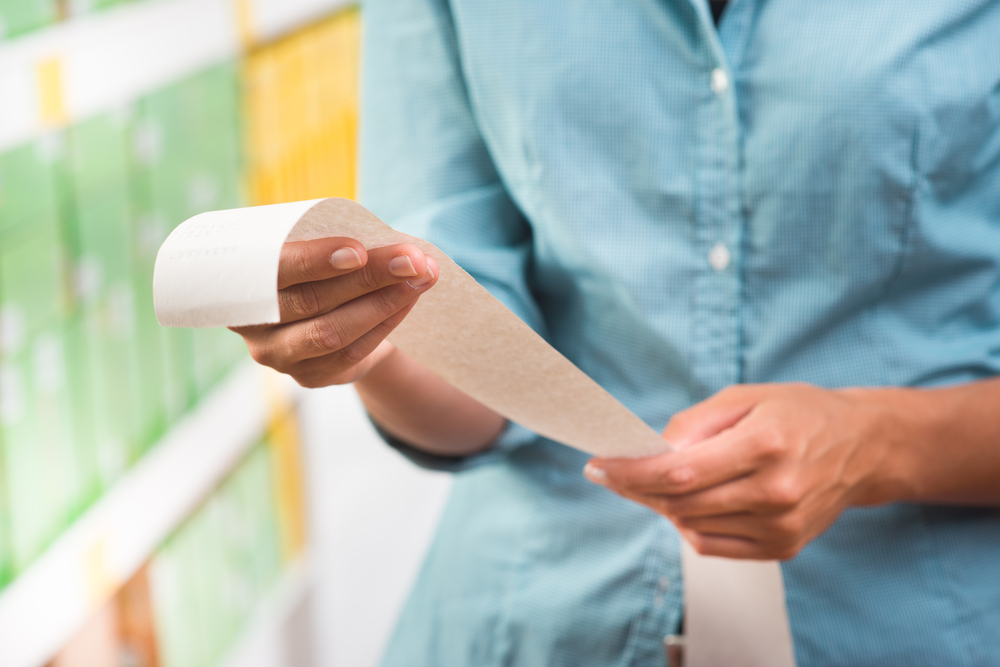 Shutterstock_210191599 Unrecognizable woman in light blue shirt checking a long grocery receipt at store.