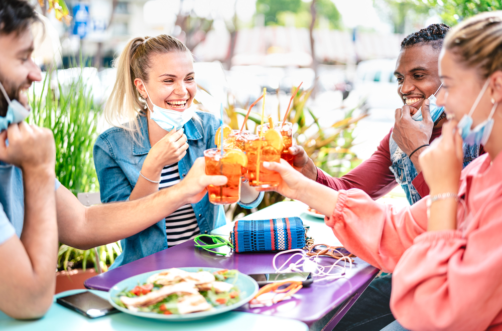 Shutterstock_1744841810 Friends drinking spritz at cocktail bar with face masks - New normal friendship concept with happy people having fun together toasting drinks at restaurant - Bright end filter with focus on left woman