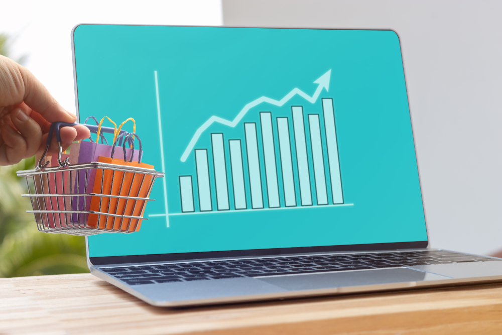 Shutterstock_1456690535 Hand holding shopping basket on laptop keyboard with graph growth and increase of chart on screen. Consumer can buy product directly anywhere anytime from seller. Online shopping and ecommerce concept