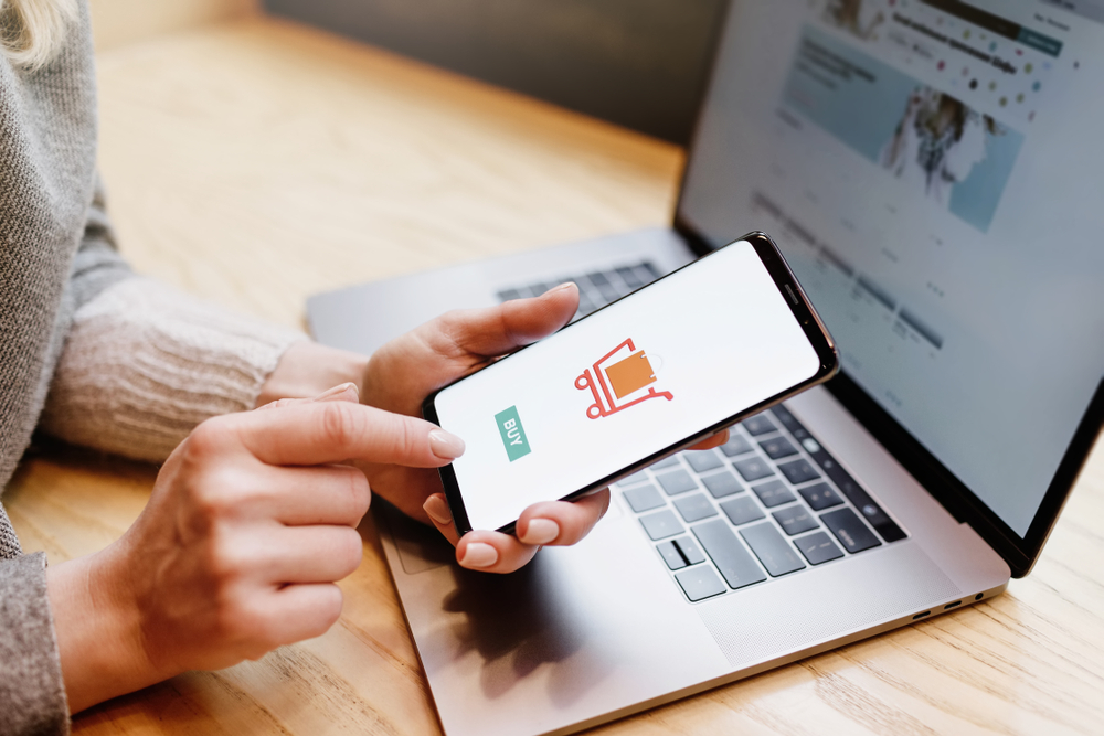 Shutterstock_1264175764 Woman with phone. Online payment. Women hands using smartphone and laptop computer for online shopping. Payment Detail page display.