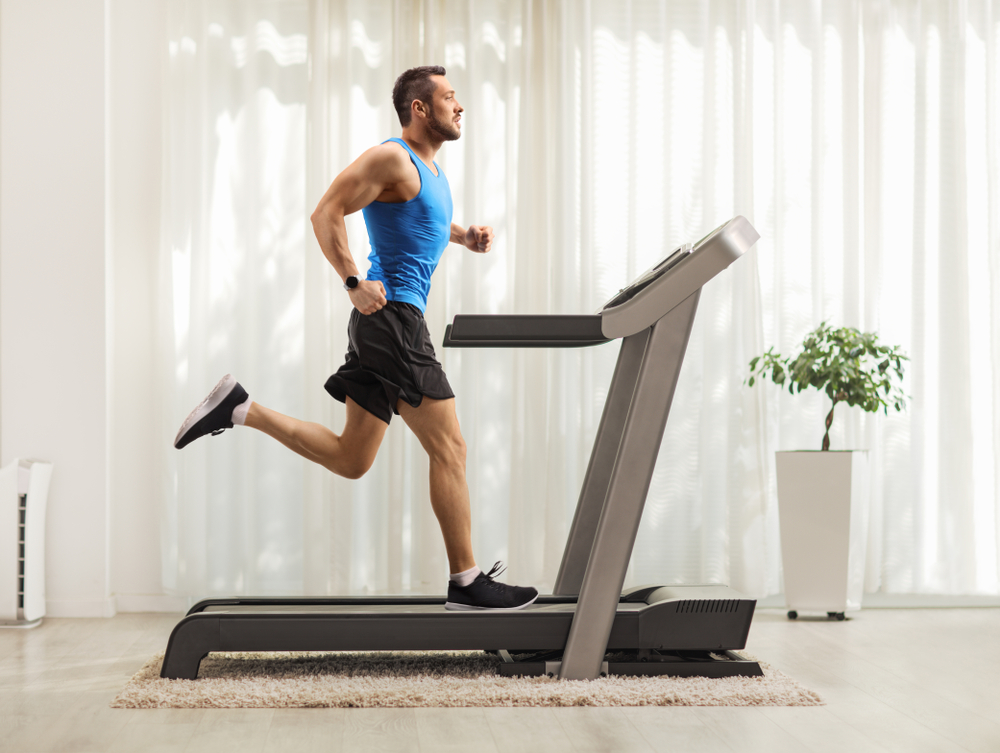 Shutterstock_1495412588 Full length profile shot of a young man running on a treadmill at home