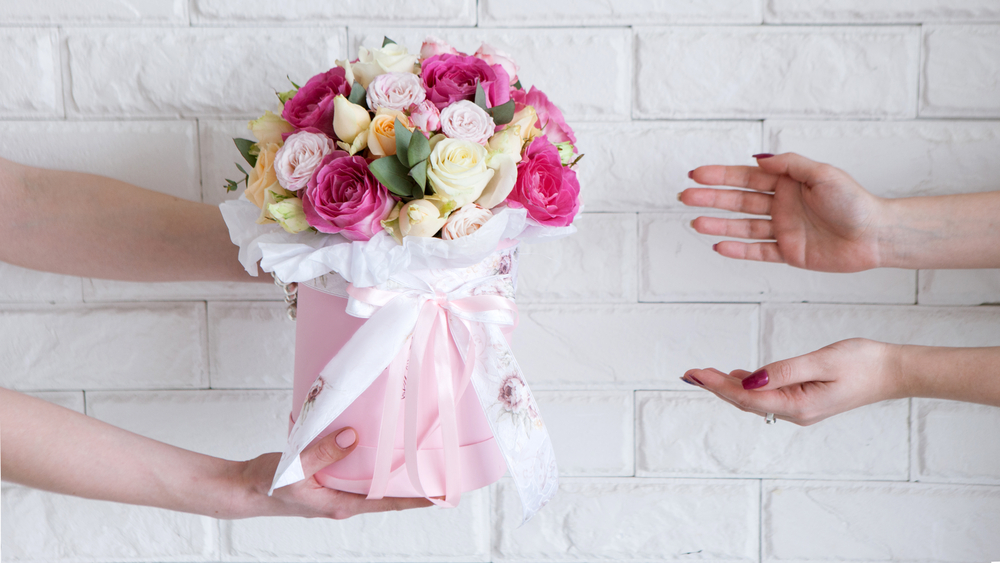 Shutterstock_648381583 Delivery of a floral workshop. The customer receives his order-a bouquet of pink and pale yellow roses. Hand courier pass flowers to the buyer