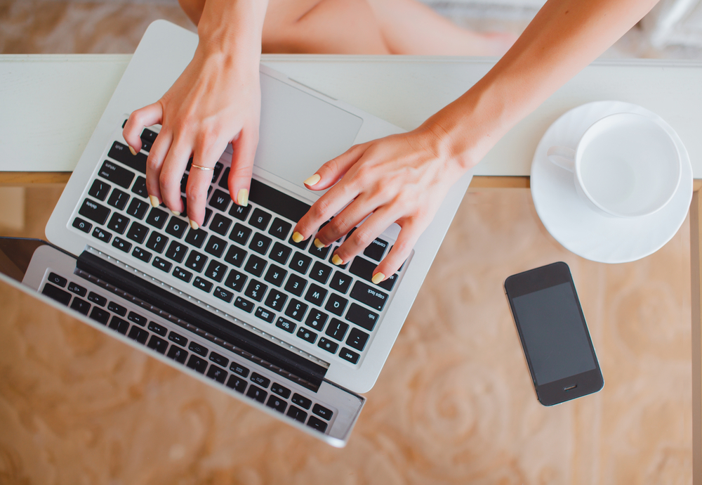 Shutterstock_302634743 young girl woman working on a laptop sitting at home write messages to drinking coffee smiling typing on a keyboard, macbook serfing, applet style, iphone,