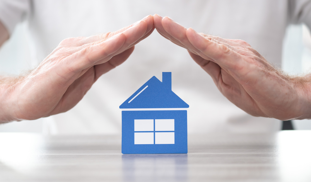 Shutterstock_1507496672 House protected by hands - Concept of home insurance