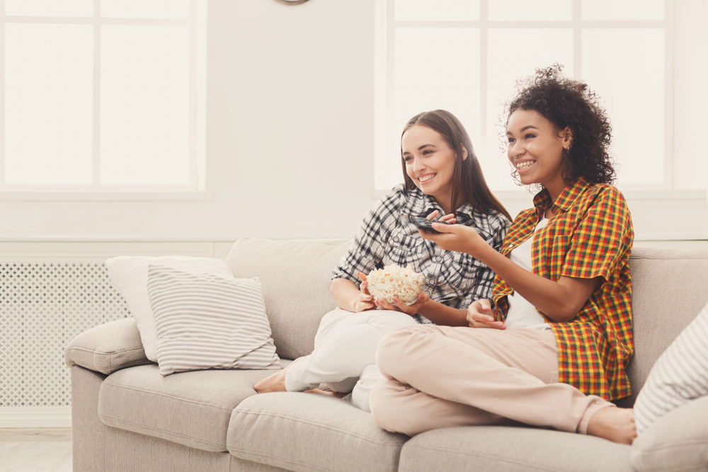 Shutterstock_790678639 Smiling young women relaxing and watching TV at home, female friends having rest after hard week, copy space