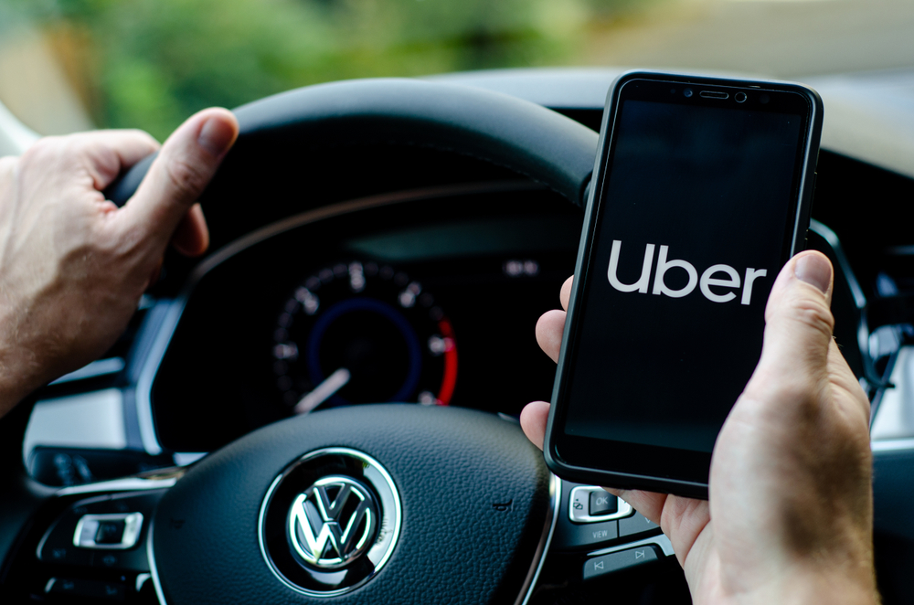 Shutterstock_1497227390 Soest, Germany - August 4, 2019: Uber driver holding smartphone in Volkswagen car. Uber is an American company offering transportation services online.